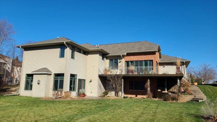 Back of a large two-story beige house with a brown deck and clear blue sky.