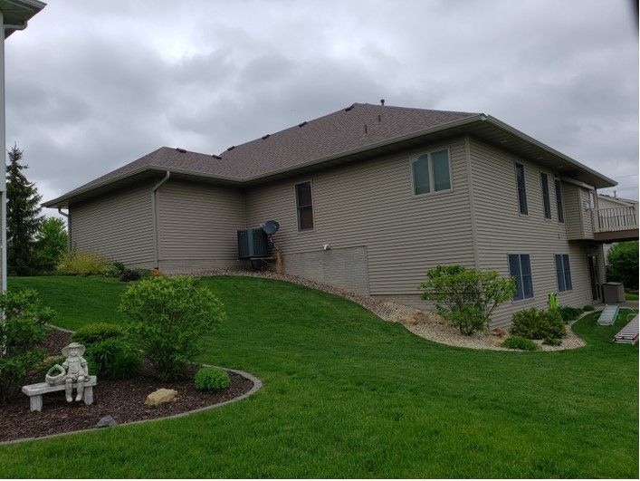Beige two-story house with brown roof and green lawn. Overcast sky.