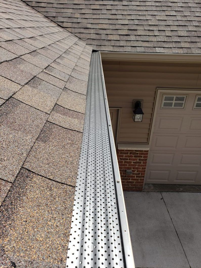 Gutter with mesh guard attached to a roof near a garage, viewed from above.