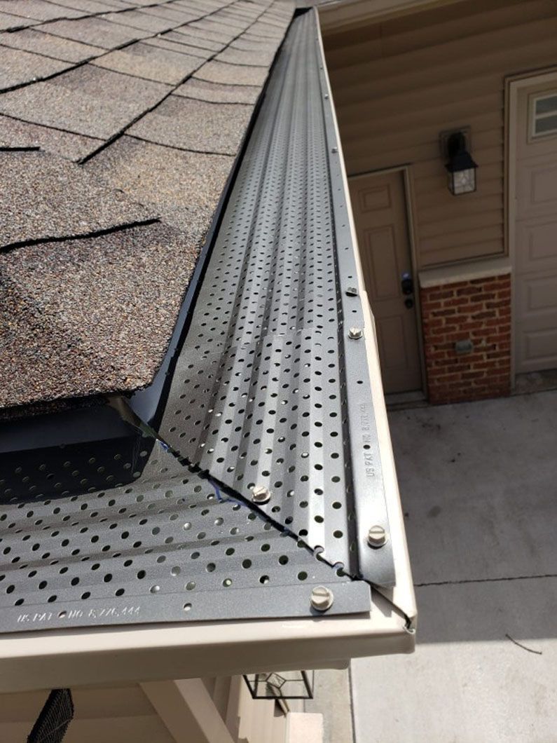 Gutter guard on a roof, protecting gutters from debris. Grey metal with perforations, against a brown roof.
