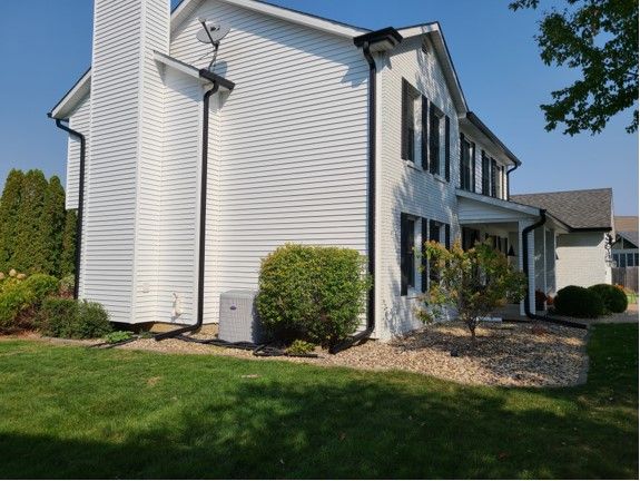 White house with black gutters and trim, green lawn, bushes, and a sunny blue sky.