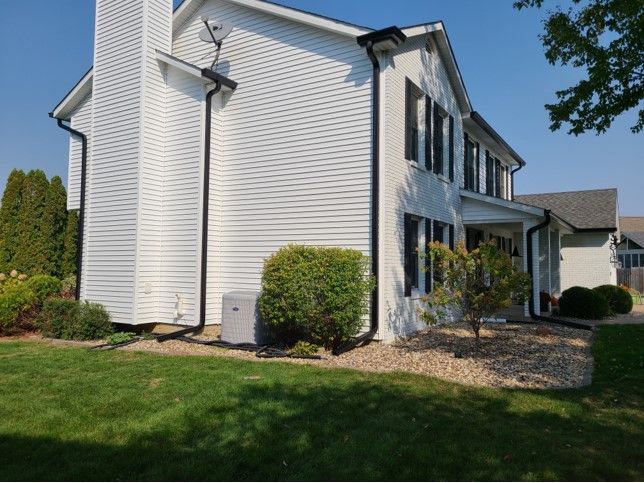 White two-story house with black shutters and gutters, a green lawn, and landscaping.