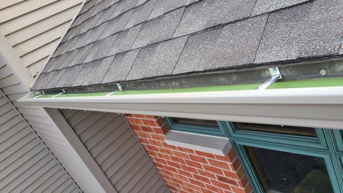 White gutter under a gray shingle roof. Green material is visible under the shingles.