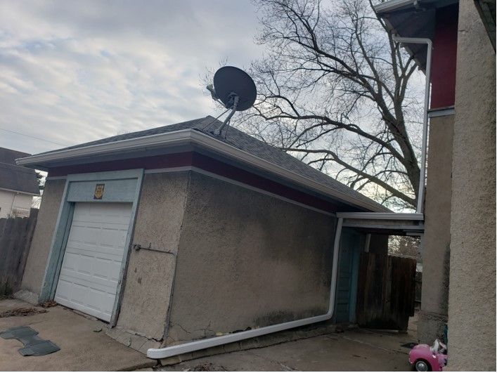 Garage with a satellite dish on the roof, a closed white door, and a connected small door on the right side.
