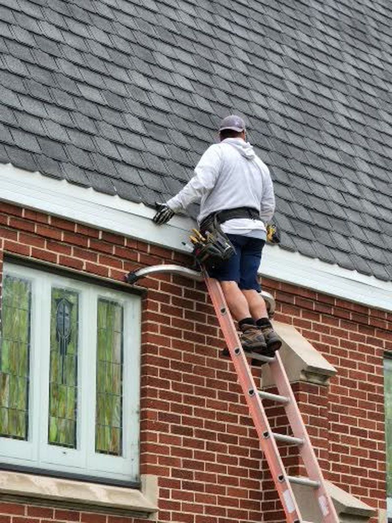 Person on a ladder cleaning gutters of a brick building.