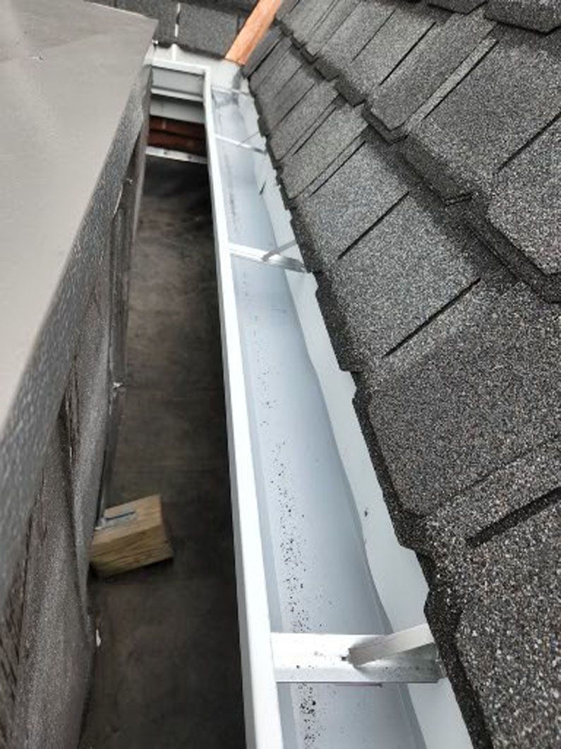 White gutter along gray roof with debris; exterior view.