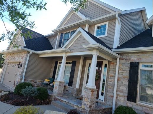 Two-story house with beige siding, stone facade, black shutters, and a front porch.
