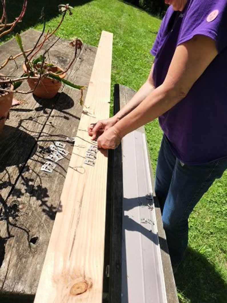 Woman in purple shirt bending wire hangers on a wooden plank outside.