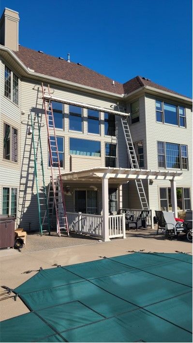 Three ladders leaning against a two-story beige house. Pool and patio furniture visible below.