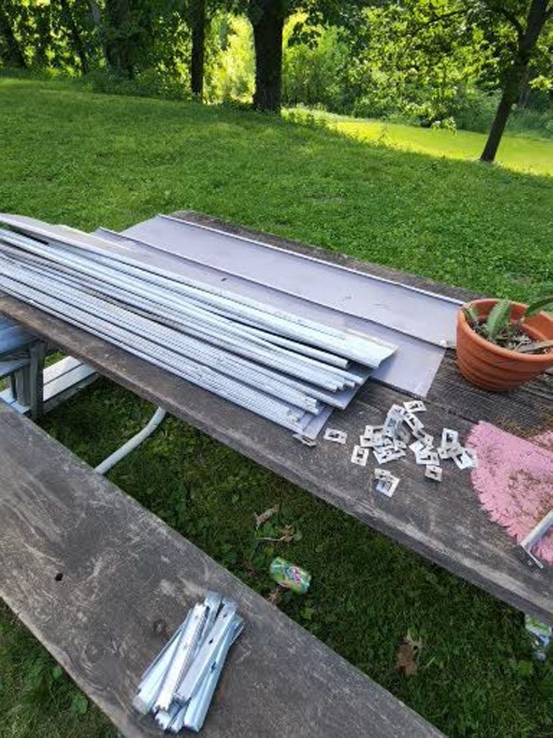 Metal siding materials and clips on a wooden picnic table outdoors, in a grassy area.