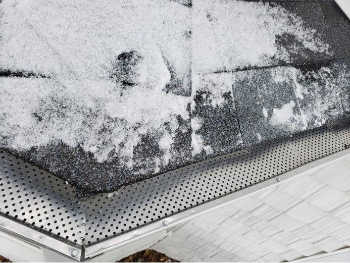 Snow-covered roof corner with a perforated gutter guard.