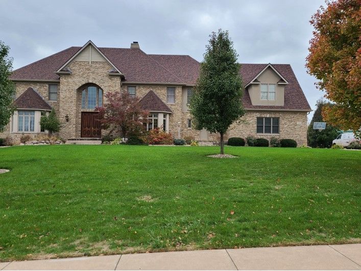 Two-story brick house with a brown roof and green lawn.
