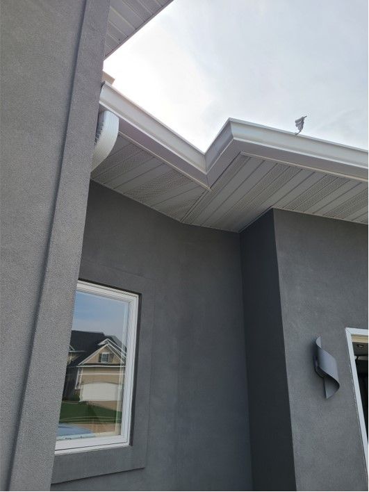Gray stucco building with white trim, gutters, and window. Overcast sky.