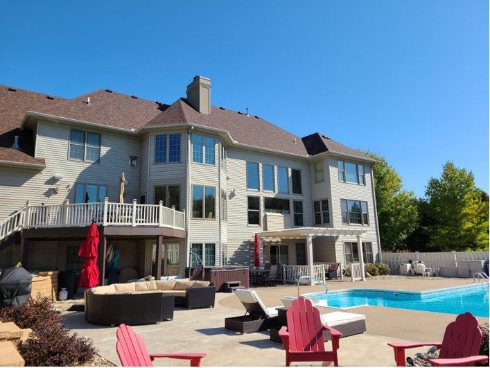 Large house with a pool, patio furniture, and a blue sky.