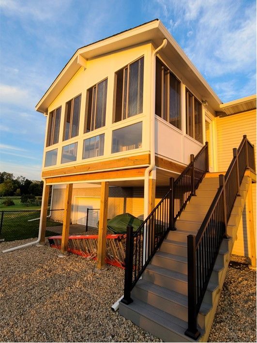 Sunroom with stairs; gray steps, black railings, white walls, and tall windows.