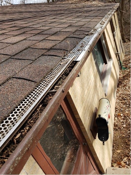 Gutter on a brown shingle roof with leaf guards. Beige building with mailbox visible.