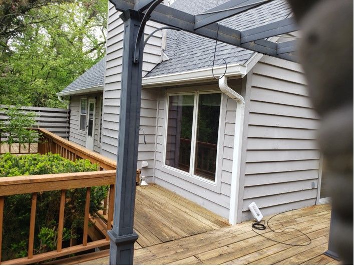 A gray house with a wooden deck and pergola. The house has a window and a gutter.