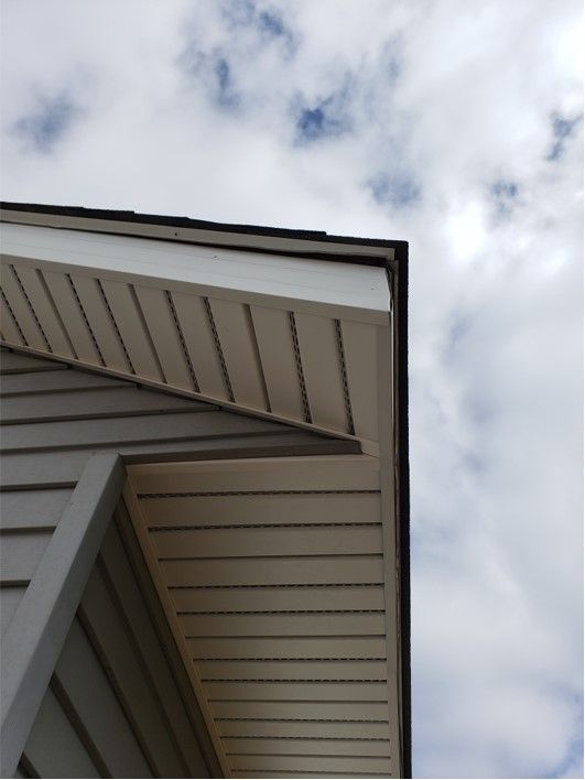 Low-angle view of a beige house exterior with a triangular roofline against a cloudy sky.