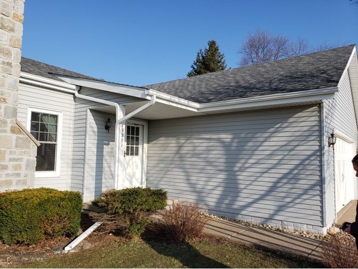 Exterior of a light gray house with white door, ramp, and shrubs under a blue sky.