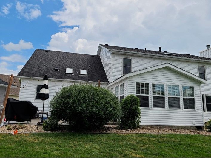 White house with a dark roof, skylights, and a sunroom; overcast sky, backyard setting.