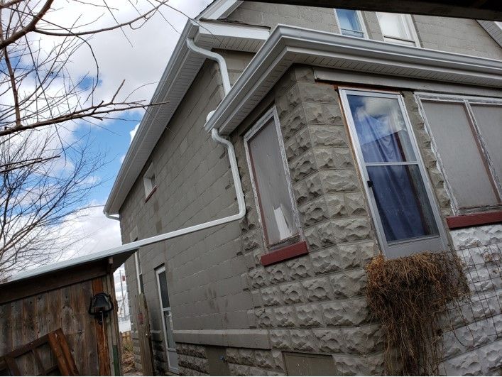 Gray brick house with white trim, gutters, and a blue sky.