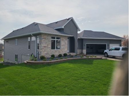Gray and stone facade house with attached garage, green lawn, and a white truck.