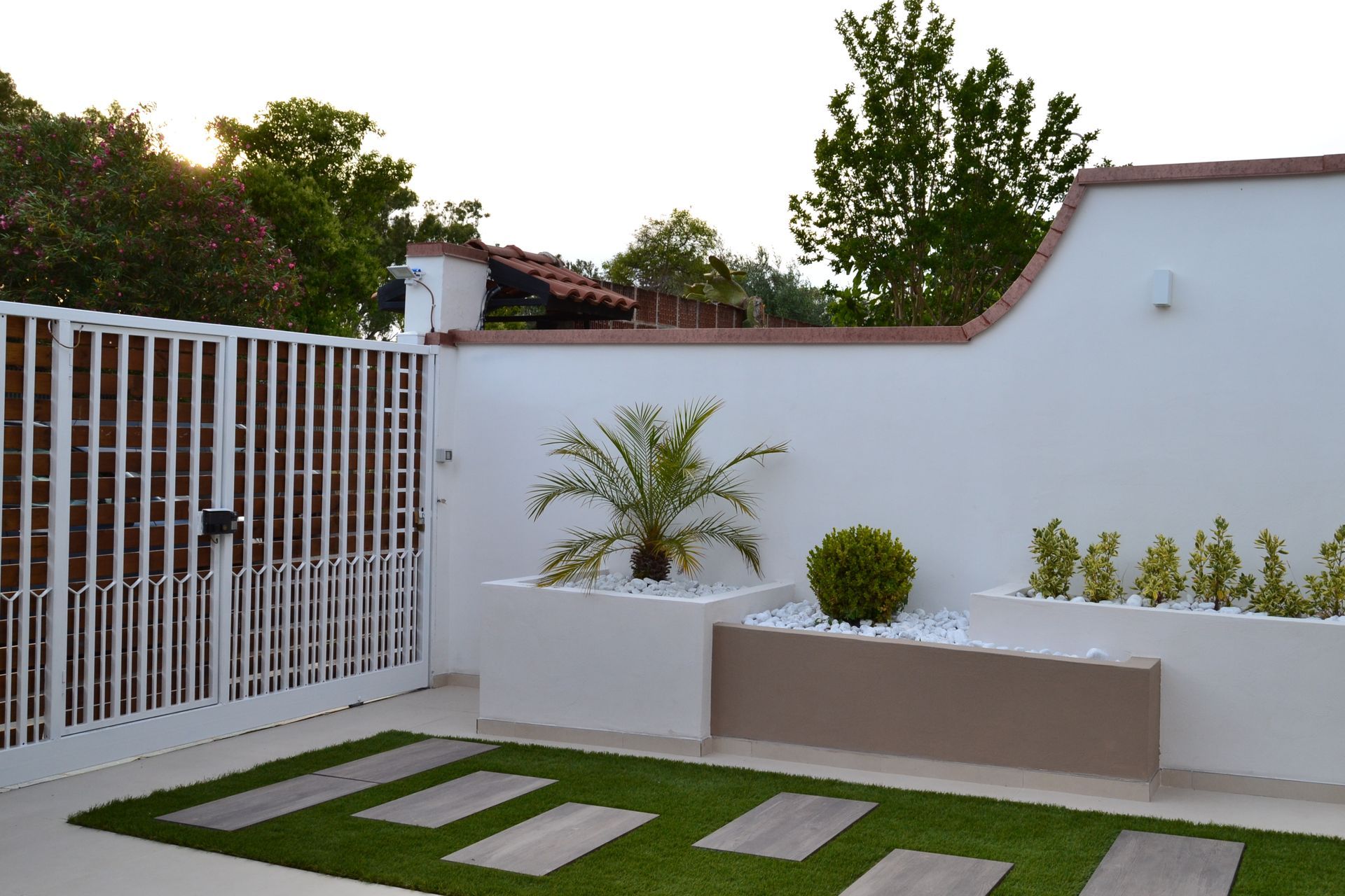Moderno patio bianco con piante in vaso, pavimentazione in pietra verde e una recinzione con cancello al tramonto
