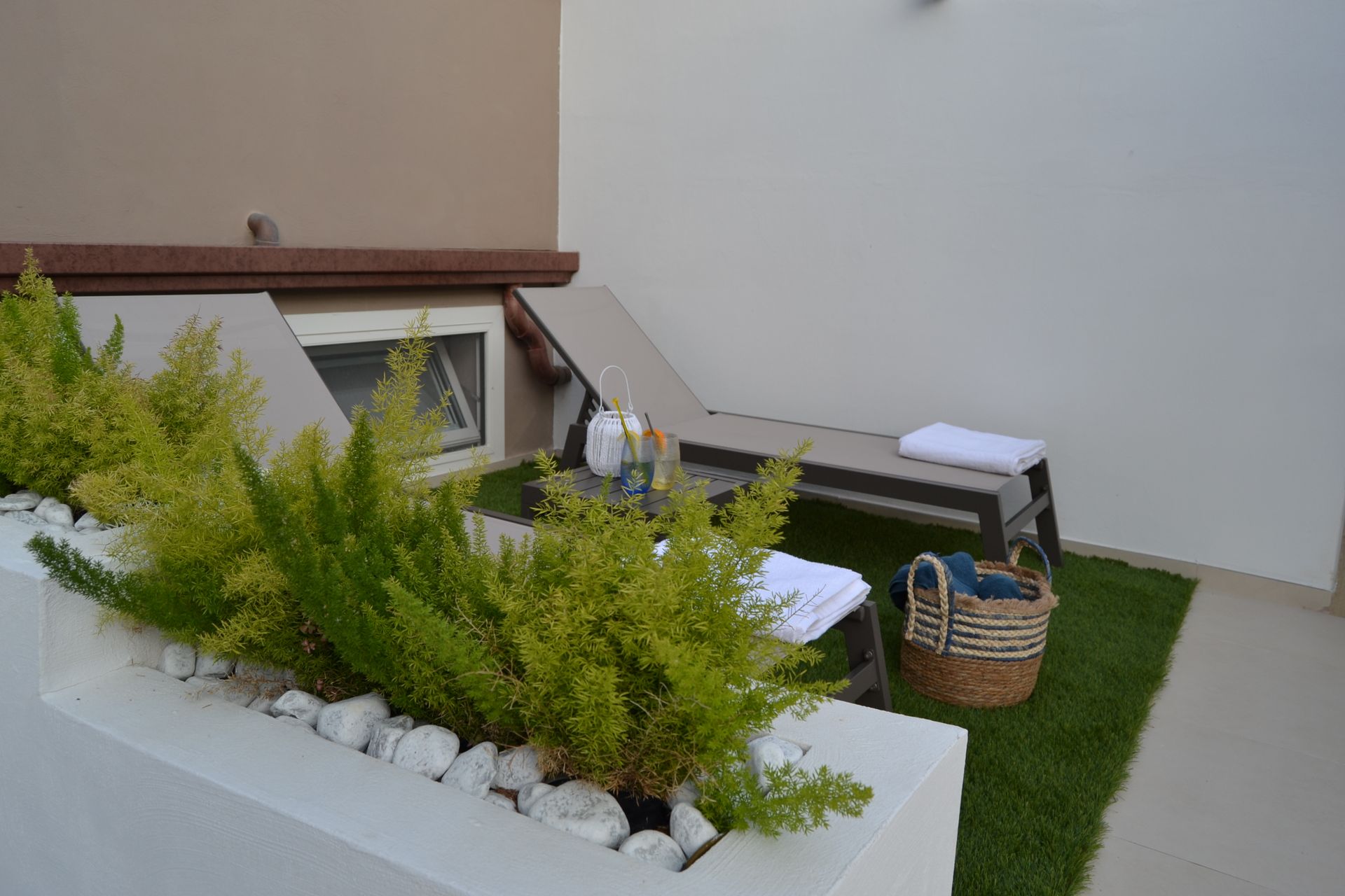 Mini patio esterno con piante in vaso, una piccola facciata di casa e un cestino da picnic su erba artificiale.