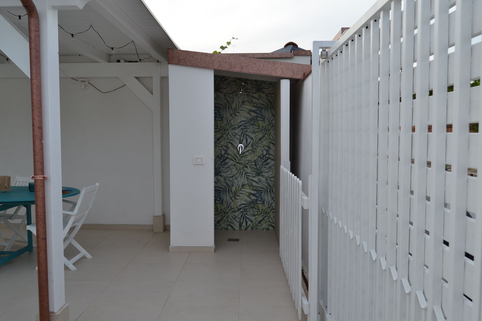 Patio coperto con pavimento piastrellato, recinzione bianca e muro ricoperto di vegetazione.