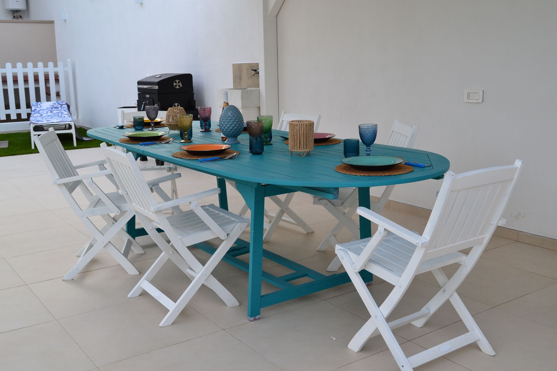 Tavolo da pranzo da esterno turchese con sedie pieghevoli bianche in una stanza luminosa