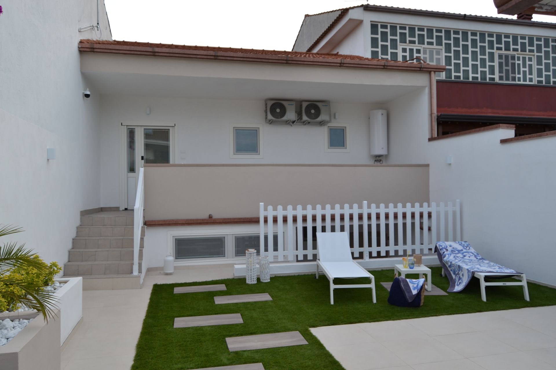 Patio sul retro con sedie a sdraio bianche, una piccola recinzione e un esterno moderno della casa.