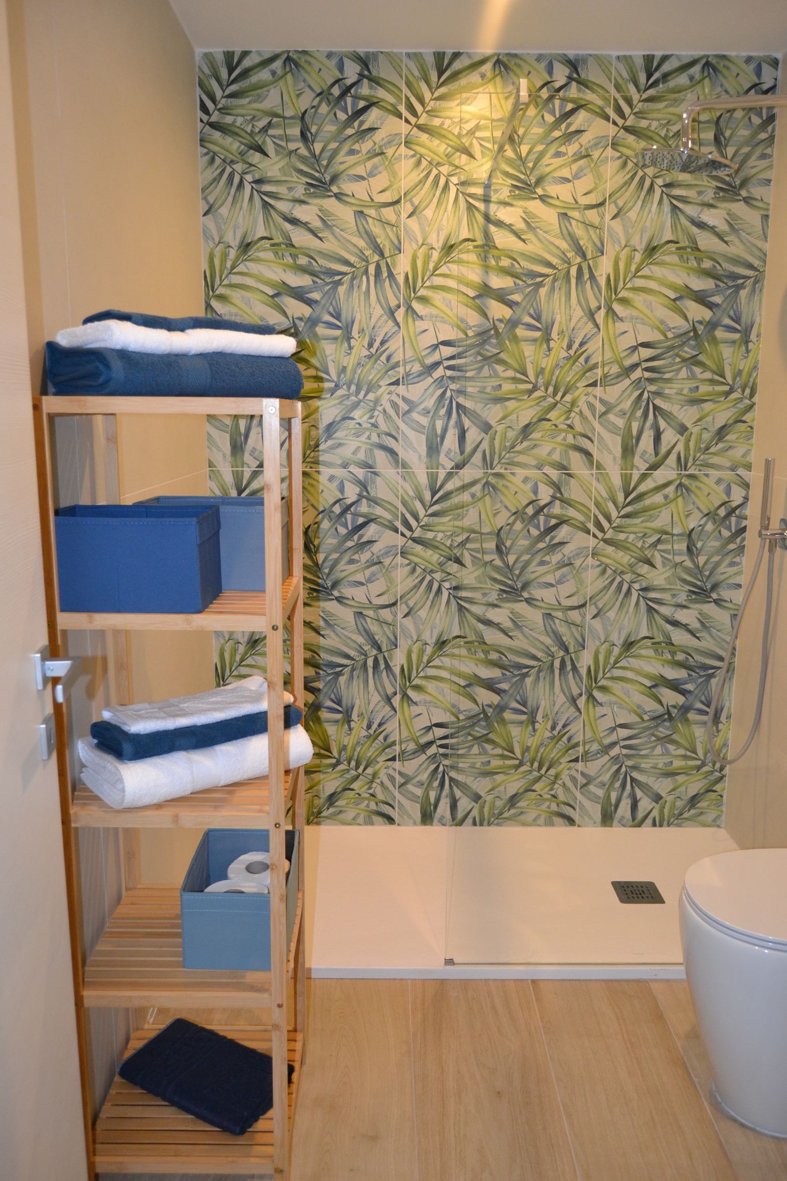 Piccolo bagno con tenda da doccia a tema tropicale, mensola e asciugamani blu accanto alla vasca e al WC.