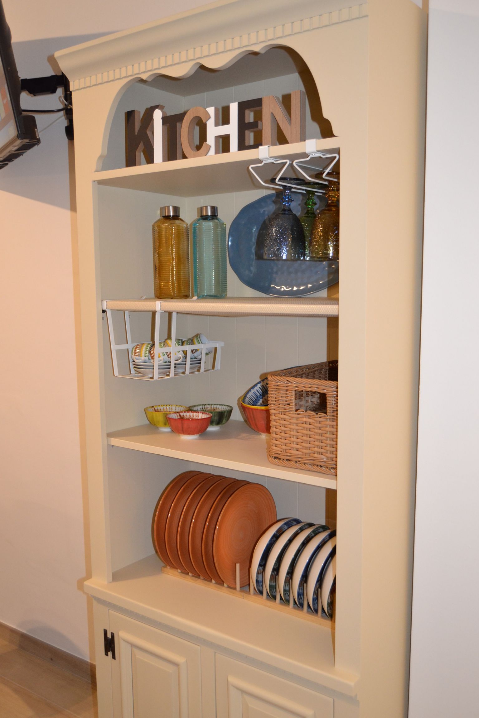 Credenza da cucina bianca con ripiani per piatti, cestini e bottiglie, con la scritta 