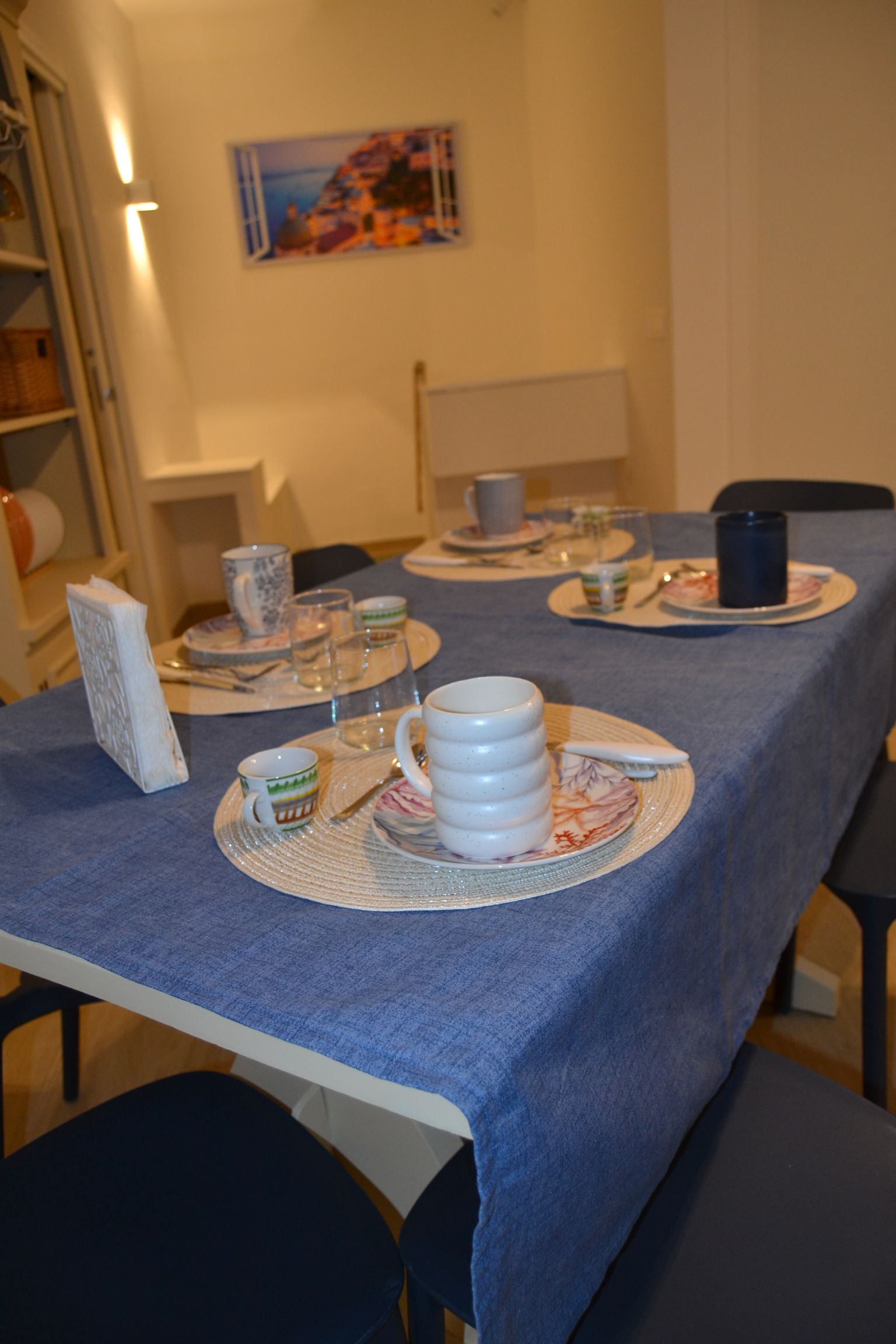 Tavolo da pranzo apparecchiato con piatti, tazze e mug su una tovaglia blu in una stanza