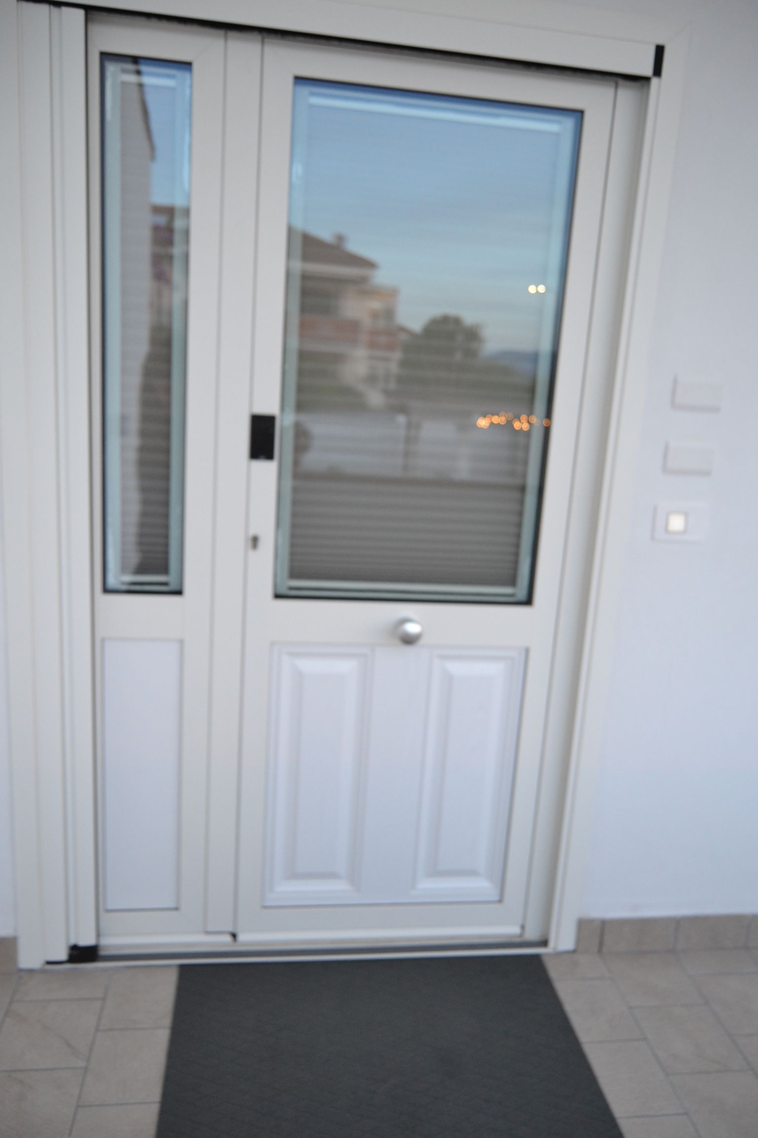 Porta d'ingresso bianca con pannelli in vetro e zerbino grigio all'entrata di un edificio