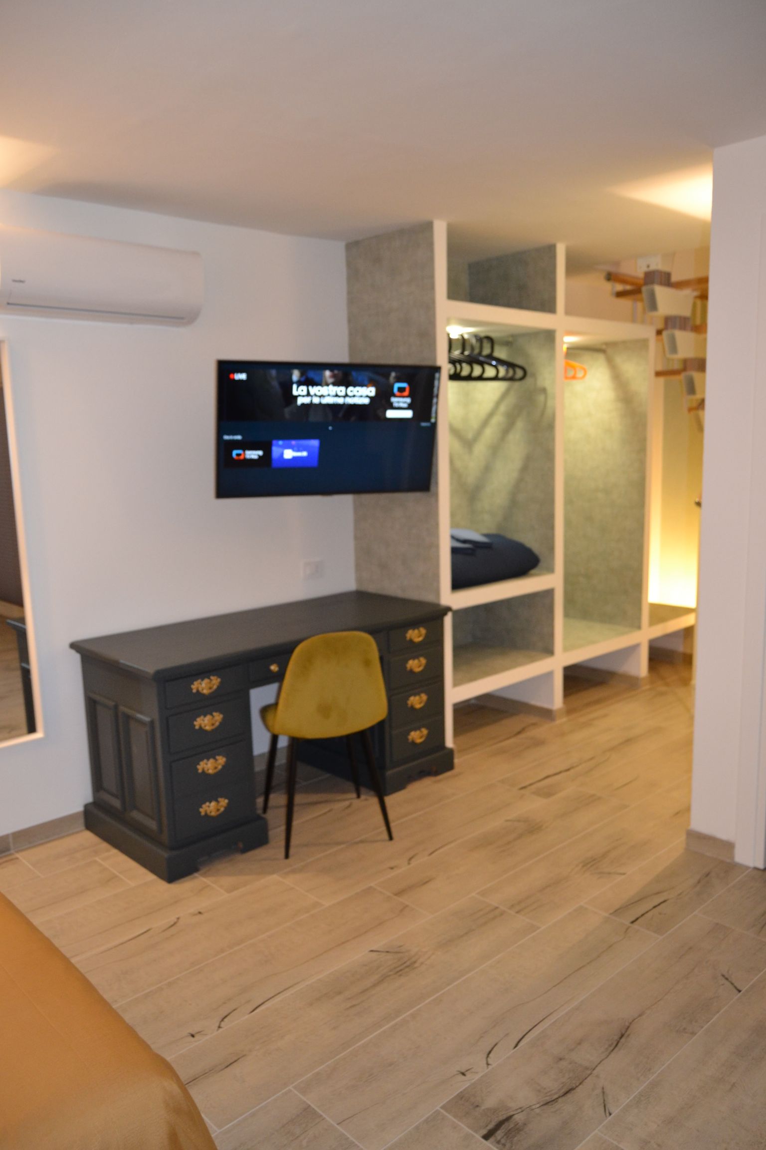 Camera da letto moderna con TV a parete, scrivania, sedia e armadio a giorno con illuminazione soffusa.