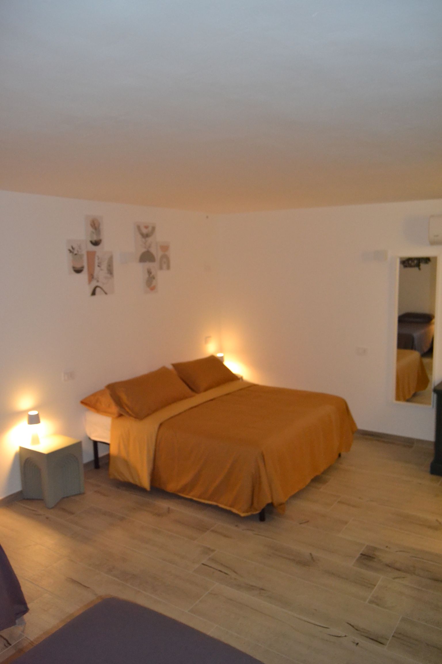 Camera da letto minimalista con copriletto arancione, lampade da comodino e decorazioni murali su pareti bianche.