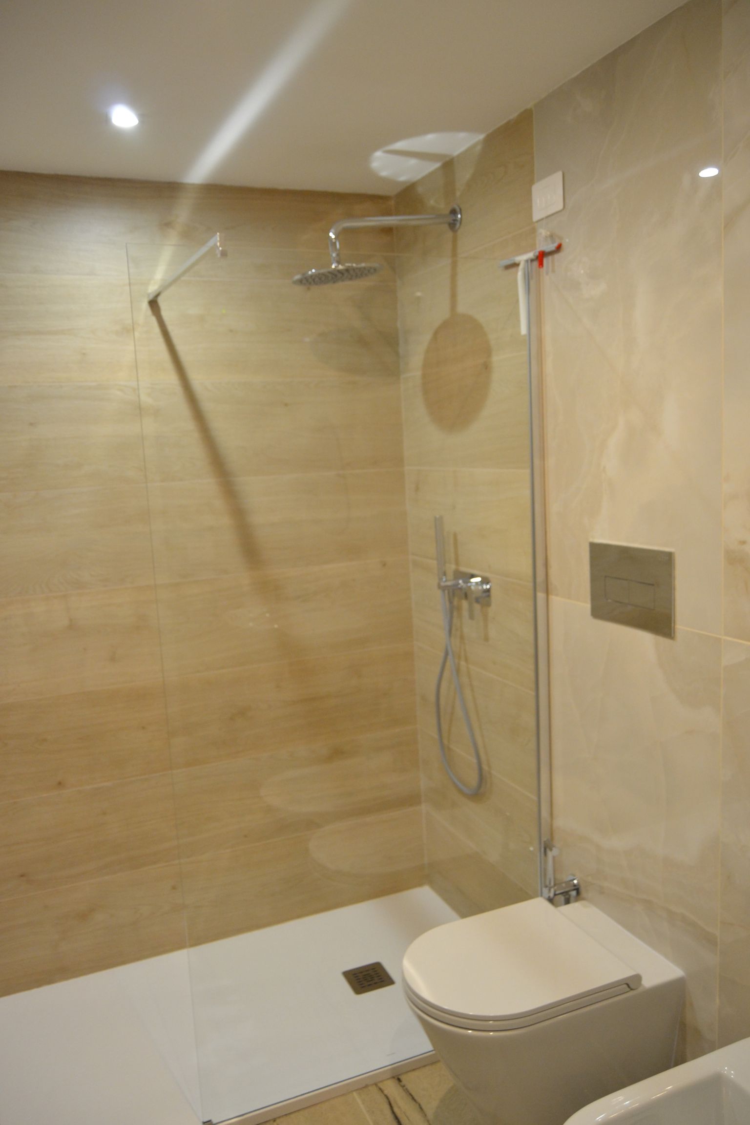 Bagno moderno con piastrelle beige, cabina doccia, doccetta a mano e WC sospeso.