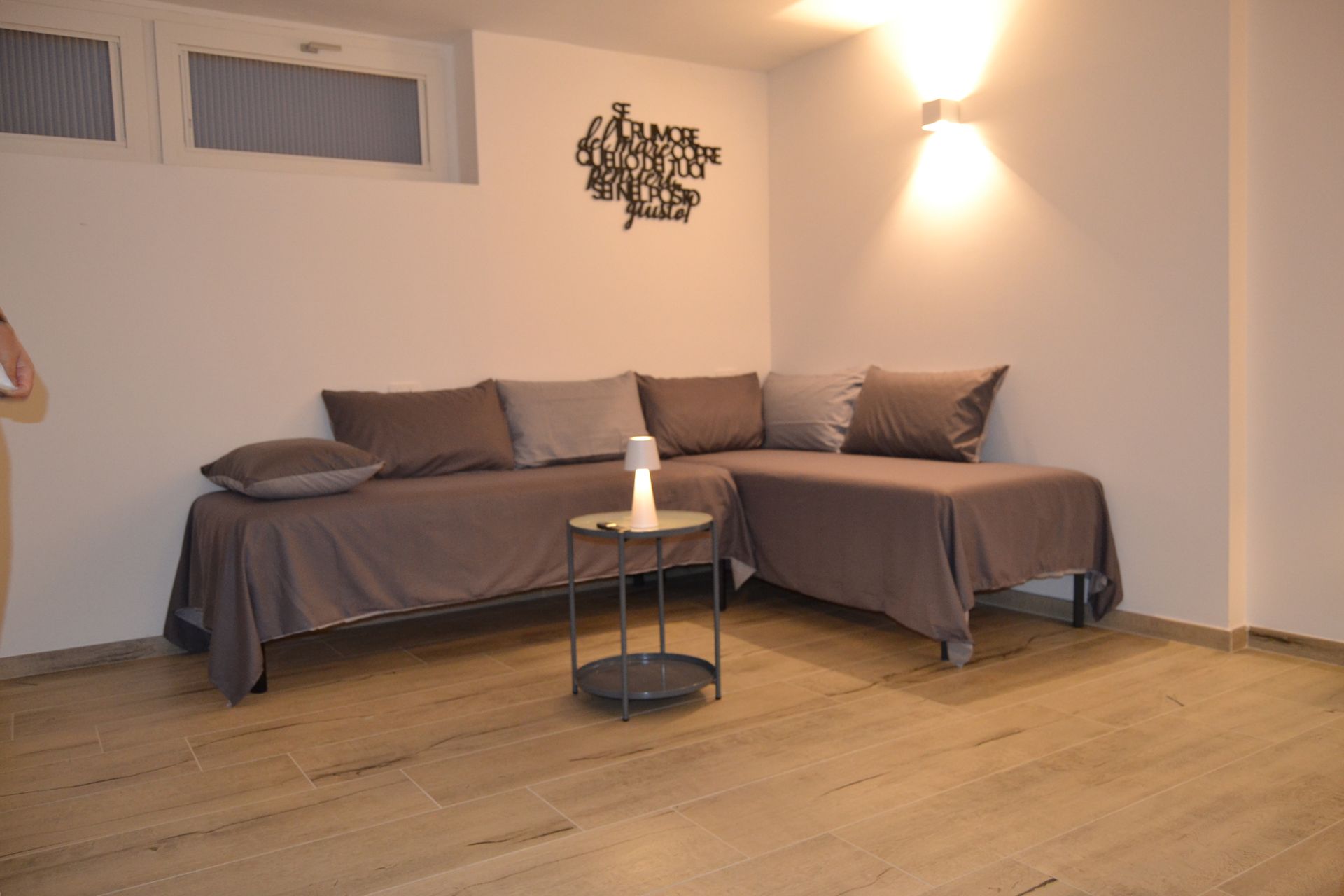 Soggiorno minimalista con divano grigio, tavolino rotondo, quadri alle pareti e illuminazione calda grazie alla lampada.