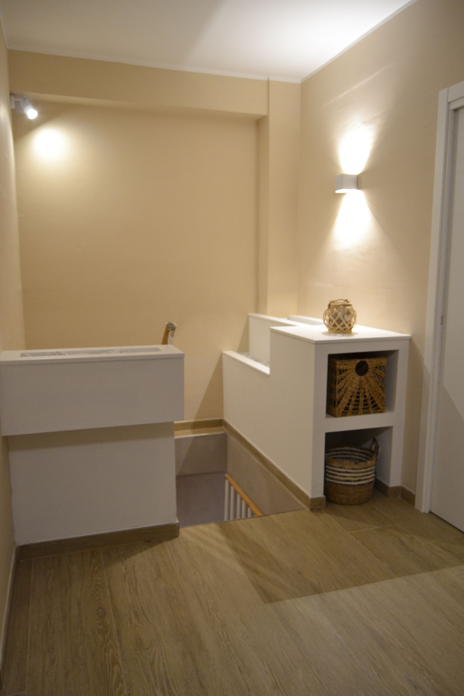Piccolo bagno beige con sanitari bianchi, applique a parete, lavabo da appoggio e una stretta apertura per le scale.