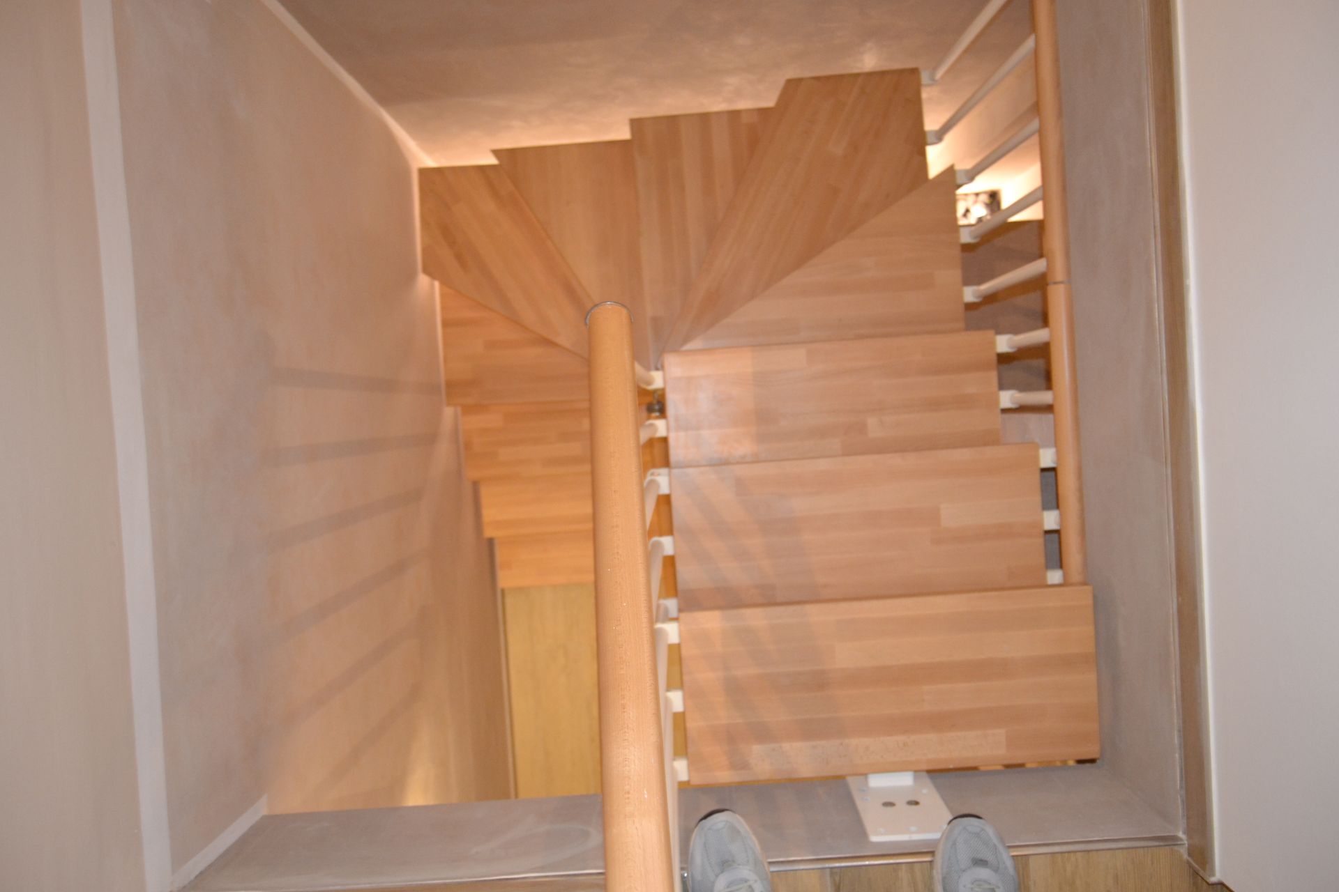 Vista dall'alto di una scala in legno in uno stretto corridoio interno, con le scarpe visibili in basso.
