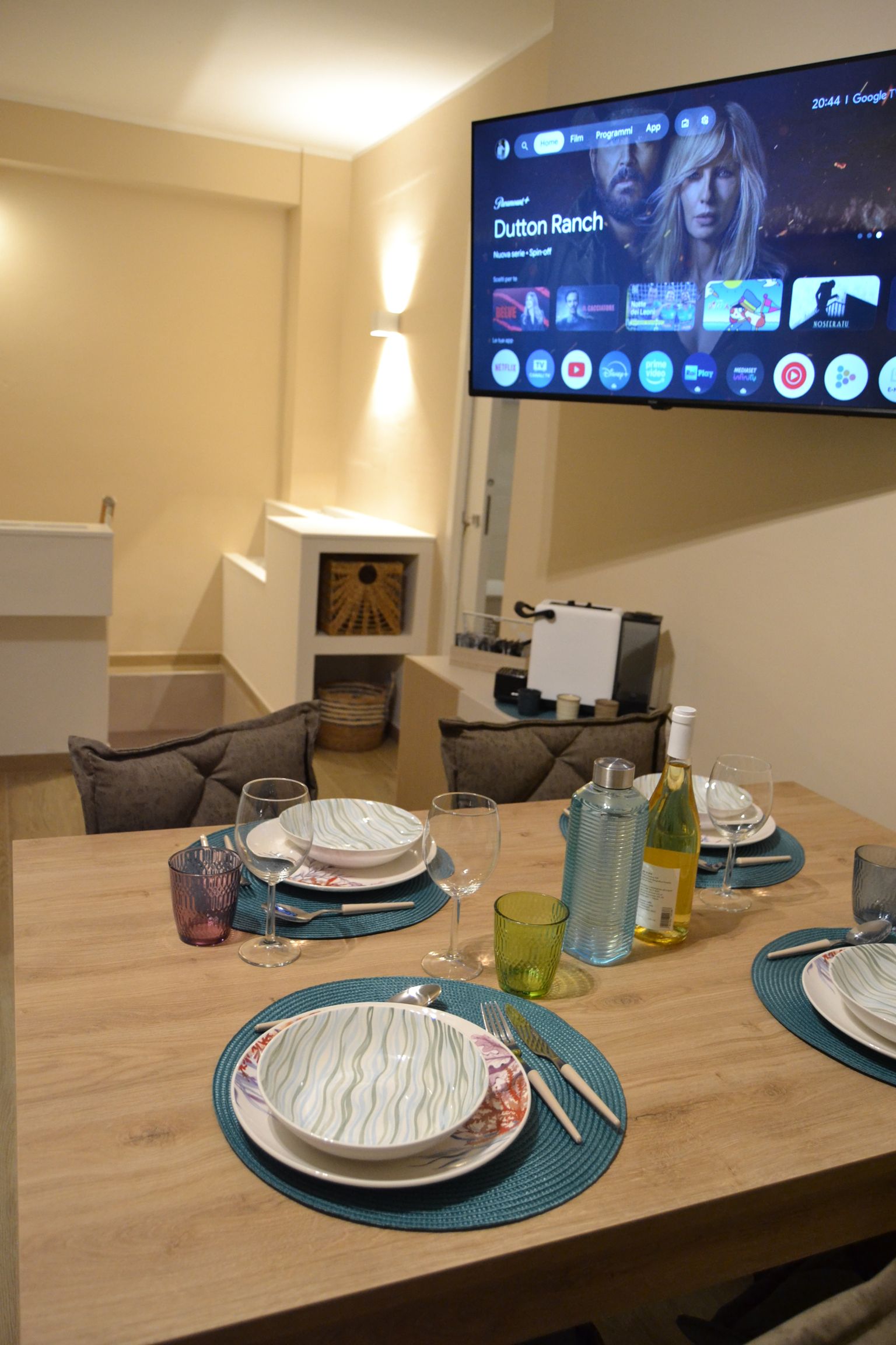 Un tavolo da pranzo apparecchiato in un accogliente soggiorno con TV montata a parete e un caminetto acceso in un angolo.