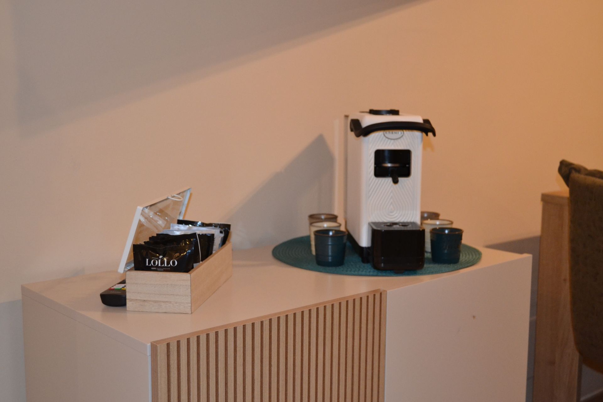 Macchina del caffè su un mobiletto con tazze e vassoio in una stanza beige.