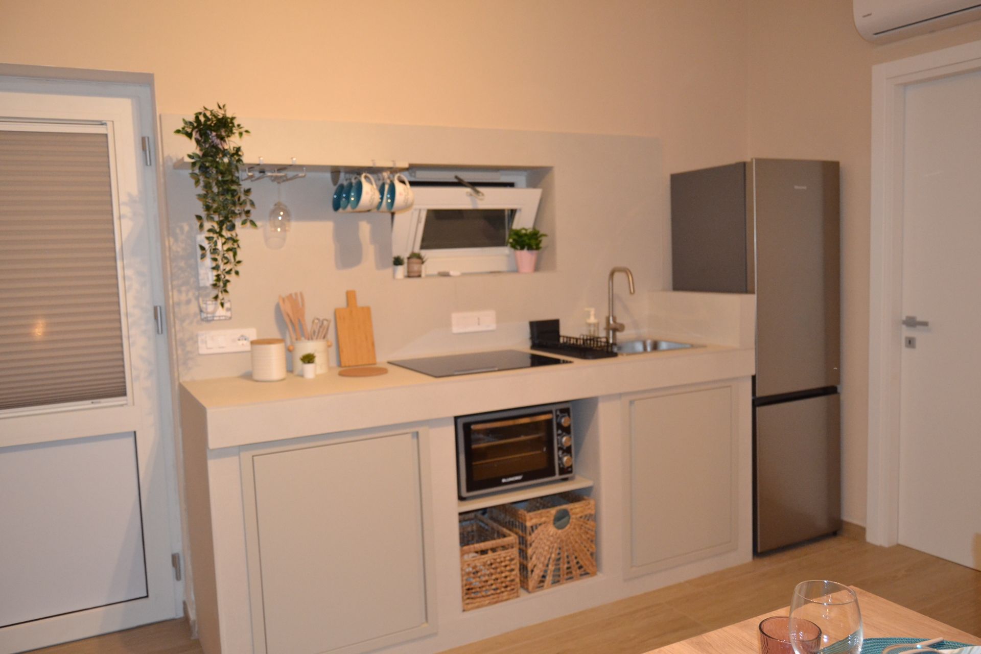 Cucina moderna con mobili bianchi, frigorifero grigio, mensole a muro e lavello da appoggio.