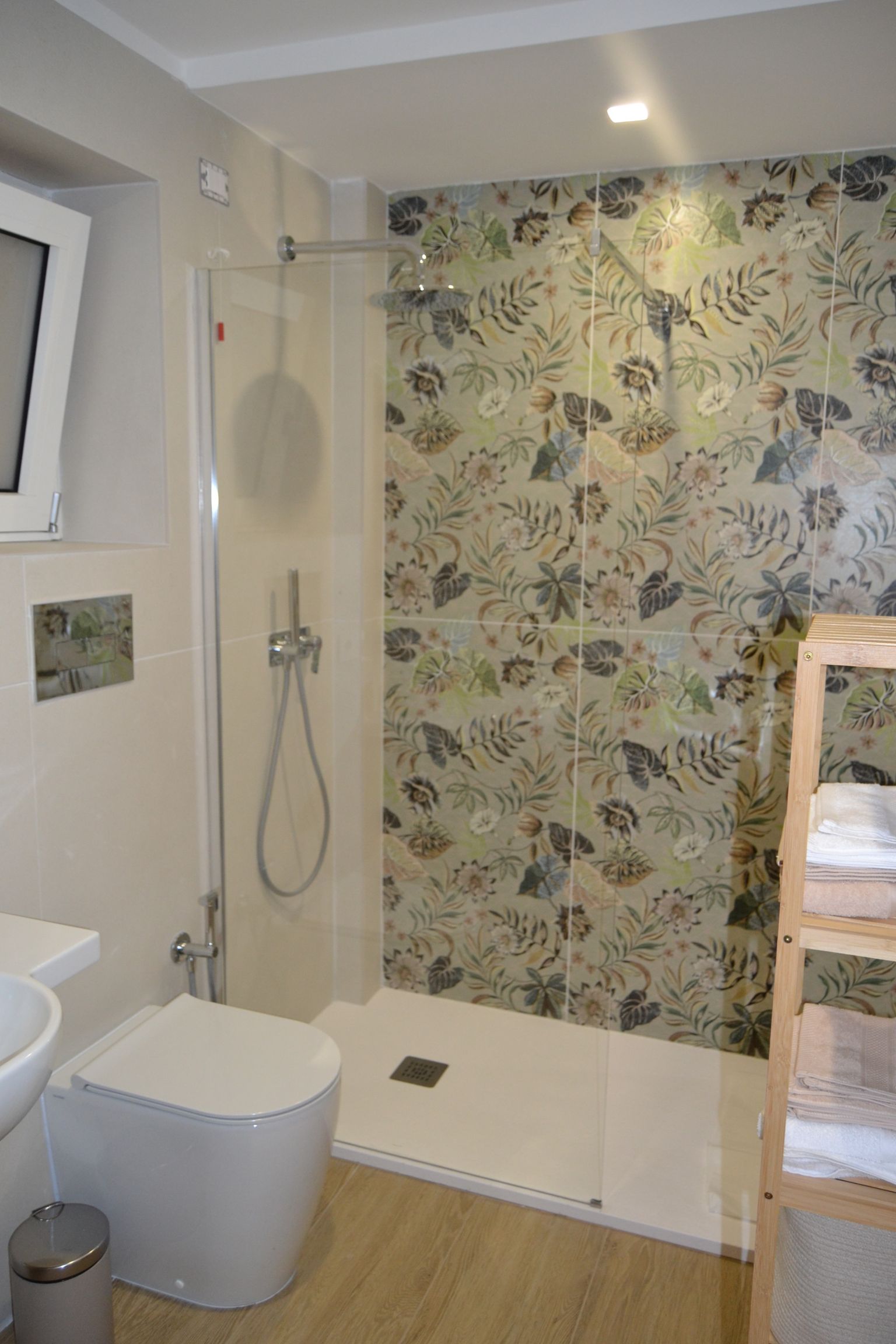 Bagno moderno con doccia, WC bianco e parete decorativa con carta da parati floreale.