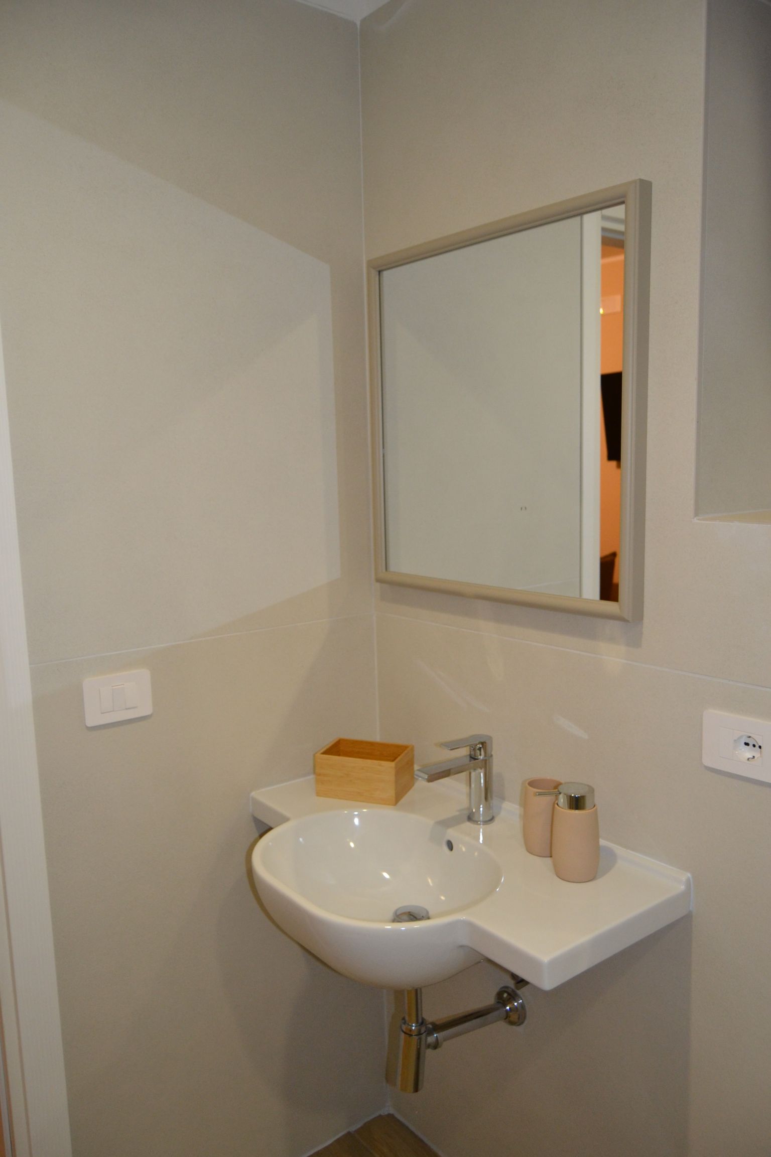 Lavabo di piccole dimensioni con specchio e dispenser di sapone su una parete bianca.