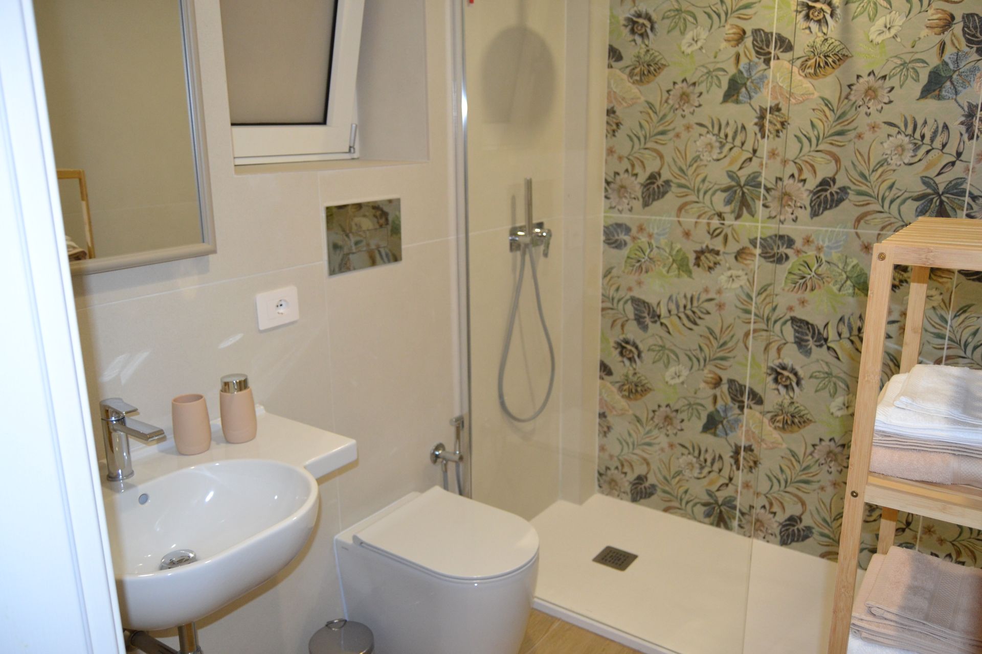 Piccolo bagno con lavandino, WC, box doccia e carta da parati a motivi floreali.