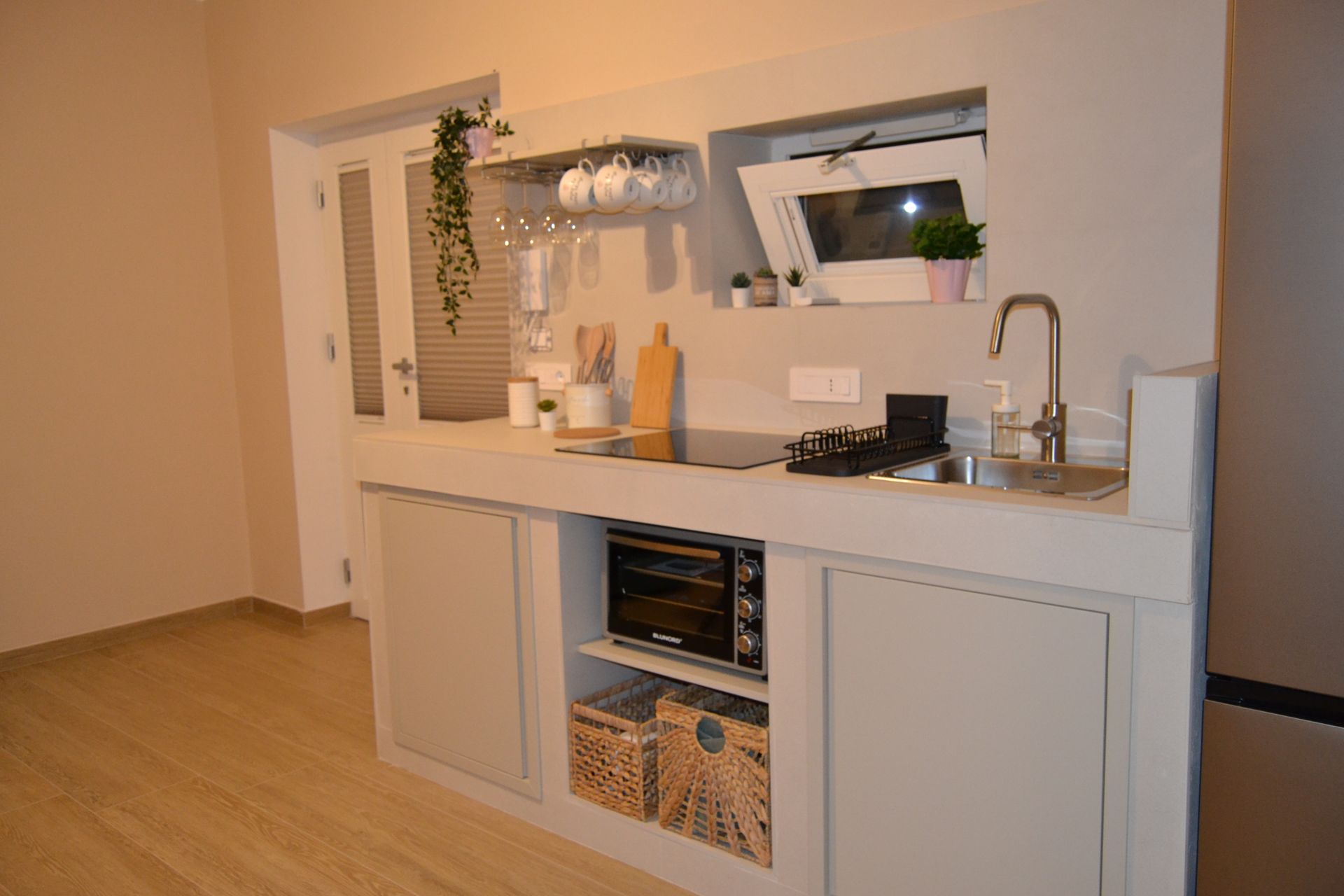 Piccola cucina moderna con mobili bianchi, lavello da appoggio, mensole a vista e pavimento in legno.
