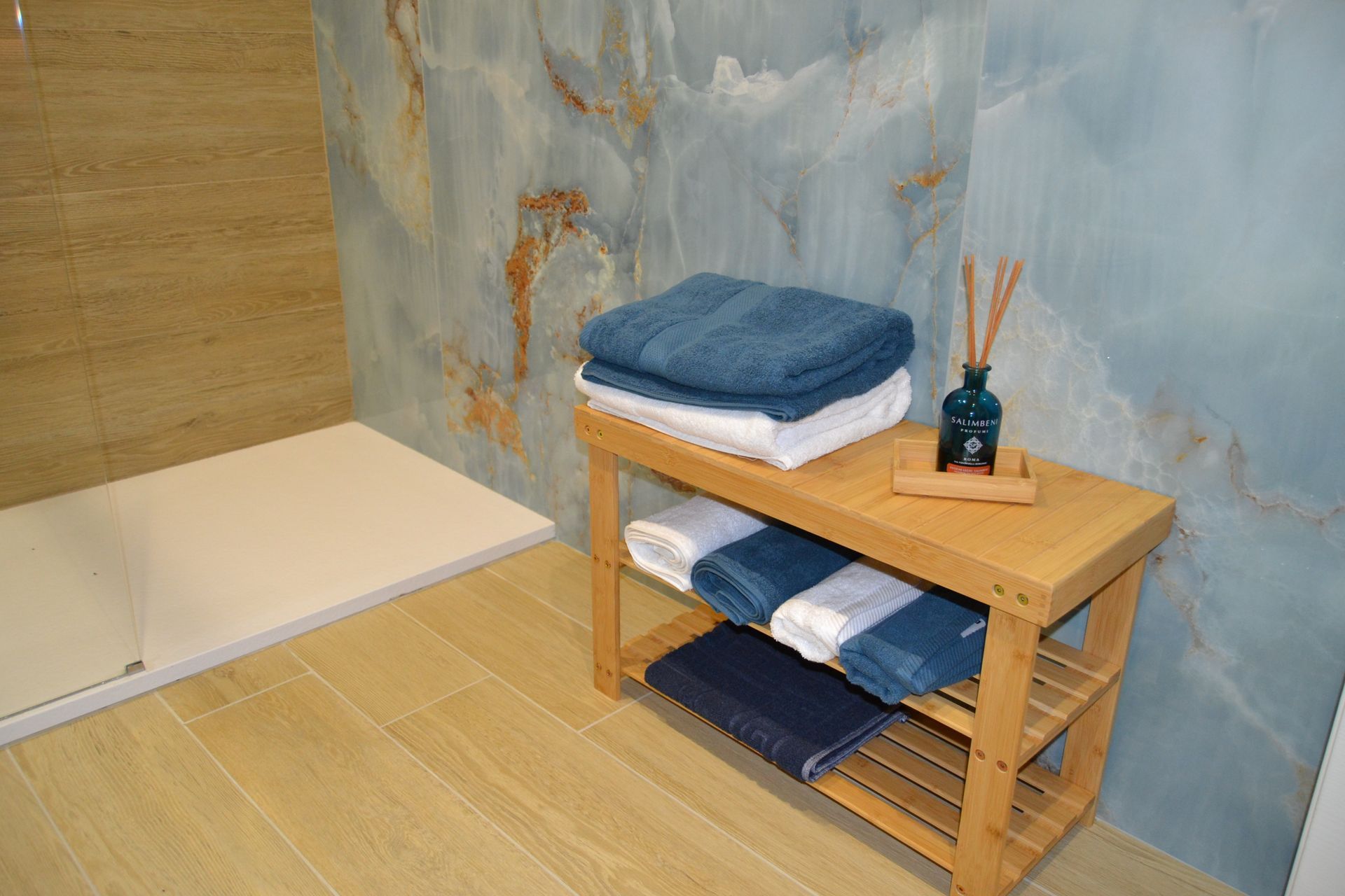 Sala spa con lettino basso e mensola in legno su cui sono riposti asciugamani blu piegati con cura e bastoncini da massaggio.