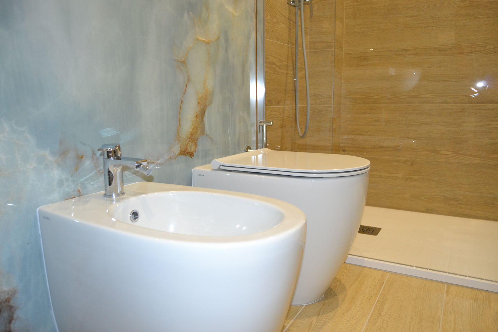 Bagno moderno con due lavandini bianchi, doccia in vetro e pareti rivestite con piastrelle effetto legno.
